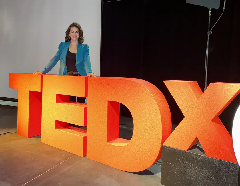 Renée Marino standing behind the TEDx letters